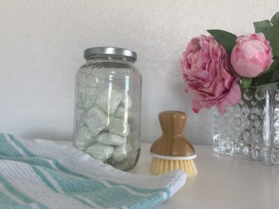 dropps tabs in glass jar with dish brush, towel, and flowers
