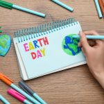 desk with markers and notebook and hand drawing an earth with text earth day on sheet
