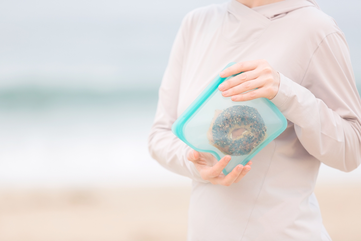 woman holding a silicone reusable sandwich bag that has a bagel in it at the beach
